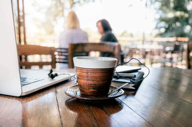 Cup of coffee and laptop on wooden table in cafe.