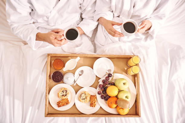 colazione fresca in camera. il primo piano della coppia sta mangiando nel letto della camera d'albergo - longtime foto e immagini stock
