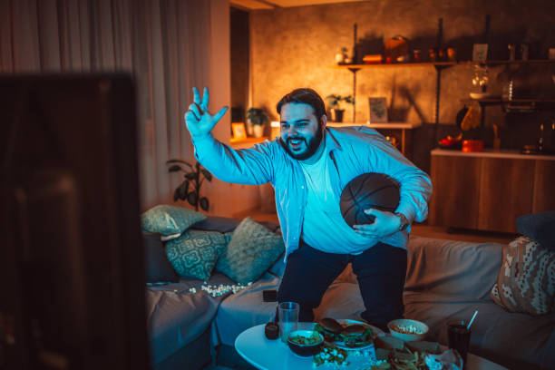 istock Fat man watching basketball 1129816984