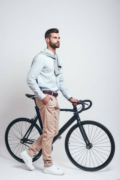 istock Convenient way to travel. Full length of a modern looking man with beard pulling his bicycle while standing in studio on a grey background 1129817076
