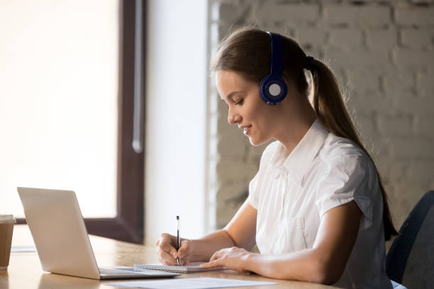 istock Focused female in headphones make notes taking online course 1129819902