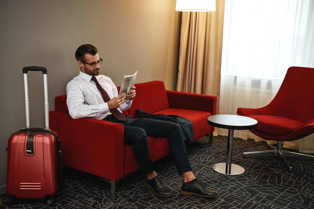 hombre de negocios spectacled con el periódico que se sienta en el sofá en pasillo del hotel - newspaper glasses the media reading fotografías e imágenes de stock