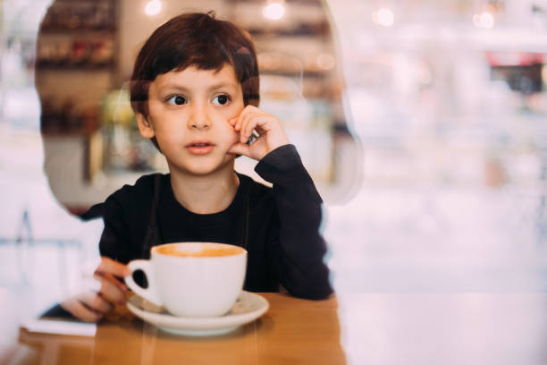 istock Little boy drinking hot chocolate at coffee shop 1129821859