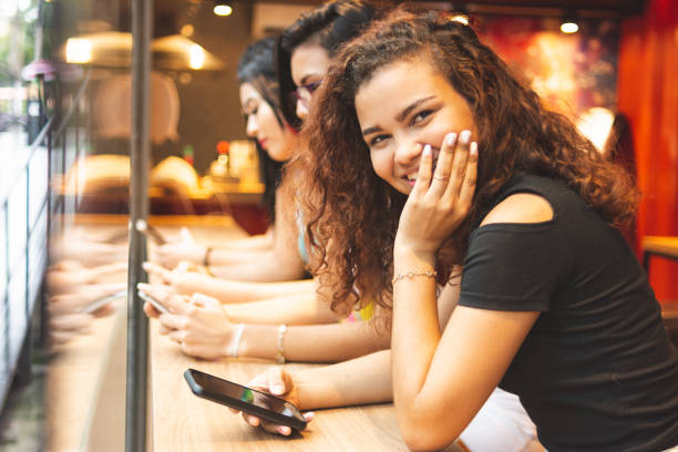 istock Brazilian girl using smartphone next to her friends, lined up at a table 1129822976