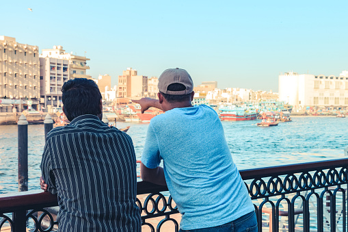 Bond, Dubai, Guide, History, Relationship - Father and Son standing near the Dubai Creek Abra Station and Having a candid conversation about Dubai's history and other tourist attractions