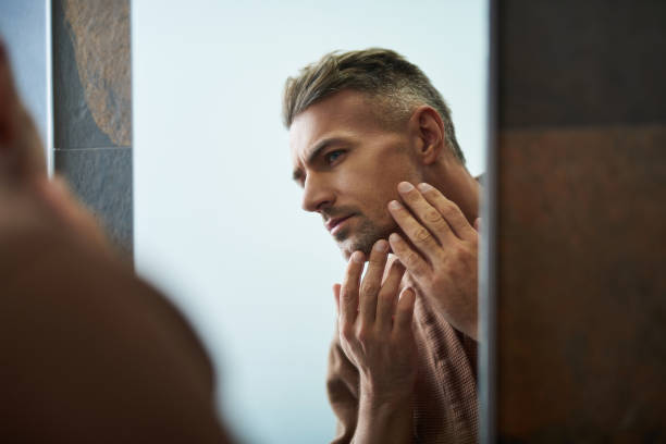 istock Handsome unshaven man looking in the mirror at home bathroom 1129826885