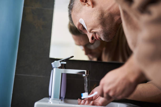 istock Handsome man with patches under eyes washing toothbrush in sink 1129826903