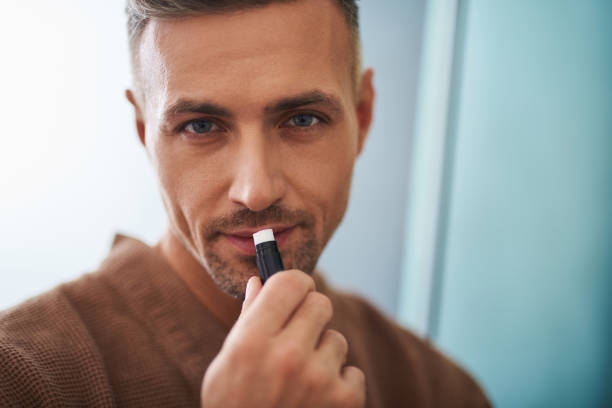 istock Handsome young man using hygienic lipstick on blue background 1129826924