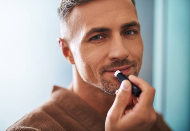 istock Attractive young man using hygienic lipstick on blue background 1129826938