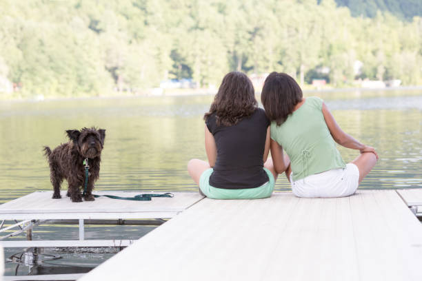 istock Two Women Sitting on The Dock with a Well behaved Dog 1129827016