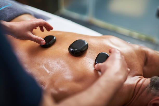 istock Professional masseur putting hot mineral stones on client back 1129831135