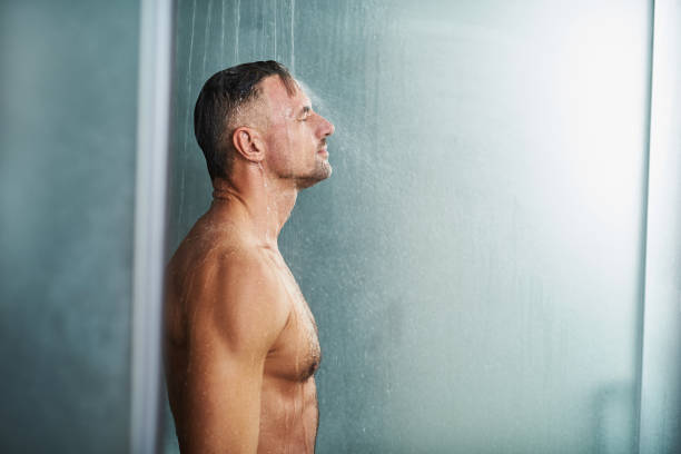 水の下で立っているハンサムな若い男が彼の体にはね値下がりしました - men naked shower bathroom ストックフォトと画像