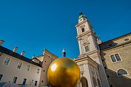 Man on the Golden Ball in Kapitelplatz (Chapter Square), beautiful sunny day view with Salzburg Cathedral (Dom zu Salzburg) on background in Salzburg, Salzburger Land, Austria.