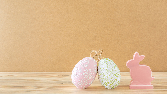 A pink bunny with two Easter eggs against a wooden background