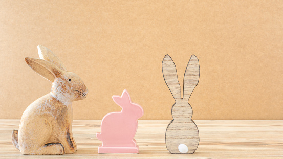 A clay rabbit, a ceramic rabbit and a wooden rabbit against a wooden background