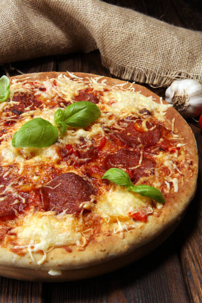 istock Italian pizza with salami, peperoni - with melted cheese, red tomatoes and green basil on a table decorated by cheese, tomato and cherry tomatoes 1129842018