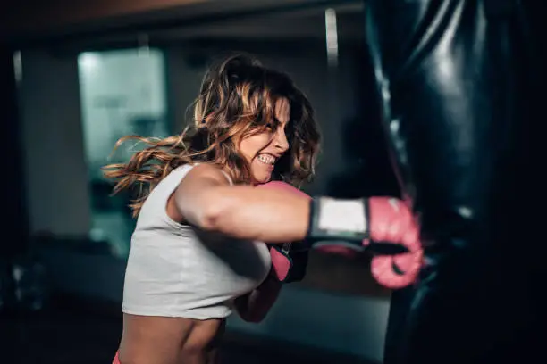 One woman, strong young lady with boxing gloves, punching a punching bag in gym alone.