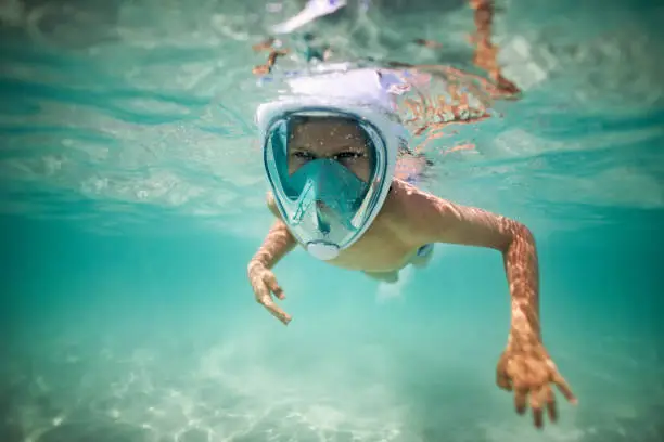 Happy little boy swimming underwater in the sea. The boy is wearing a modern full-face snorkel mask.
Nikon D850