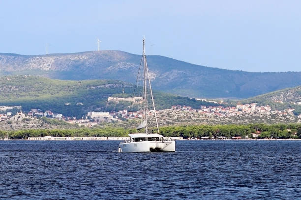 航行のカタマラン バミューダ スループ型リグで現代のクルーズは、日当たりの良い夏の日にクロアチアのリビエラのグリーン海岸過去行きます。地中海のアドリア海。ダルマチア地方 - riff ストックフォトと画像