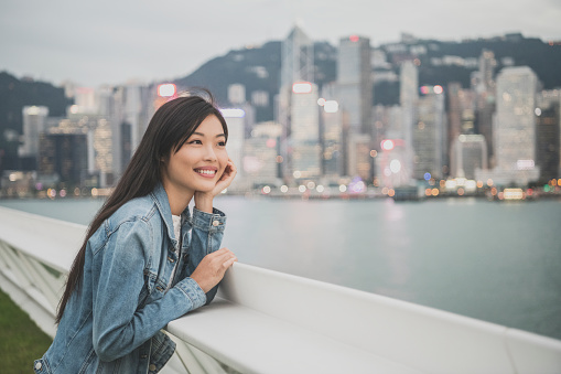 Young Chinese tourist in her 20s looking at views across the river, city in distance, smiling, sightseeing, weekend activity