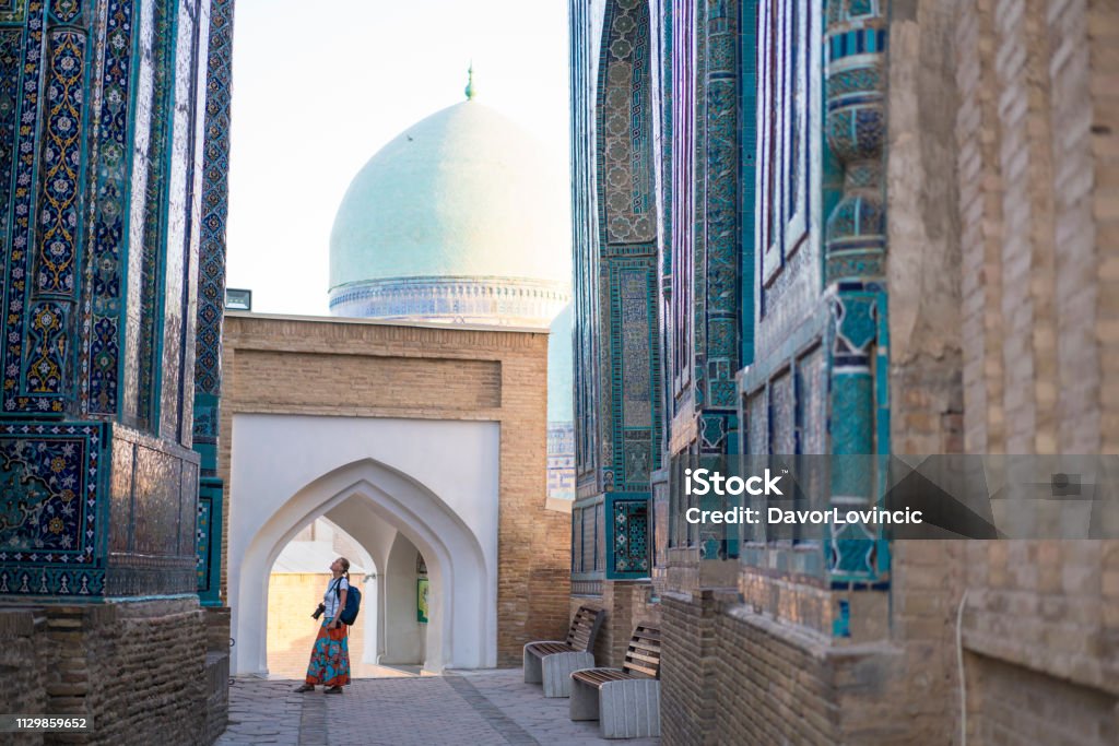 Senior woman at memorial buildings of Shah-I-Zinda Mausoleums in Samarkand, Uzbekistan Senior woman on the path between memorial buildings of Shakhi Zinda  Mausoleum which is memorial complex of Islamic architecture from 9 to 12. century in Samarkand, Uzbekistan Uzbekistan Stock Photo