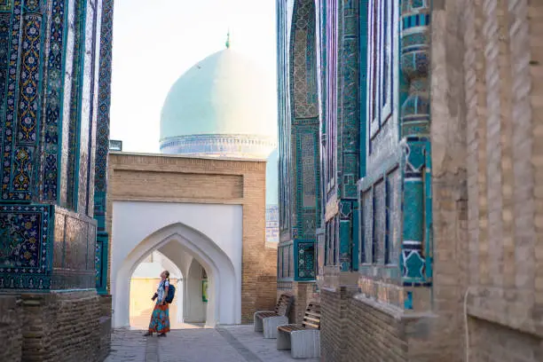 Senior woman on the path between memorial buildings of Shakhi Zinda  Mausoleum which is memorial complex of Islamic architecture from 9 to 12. century in Samarkand, Uzbekistan