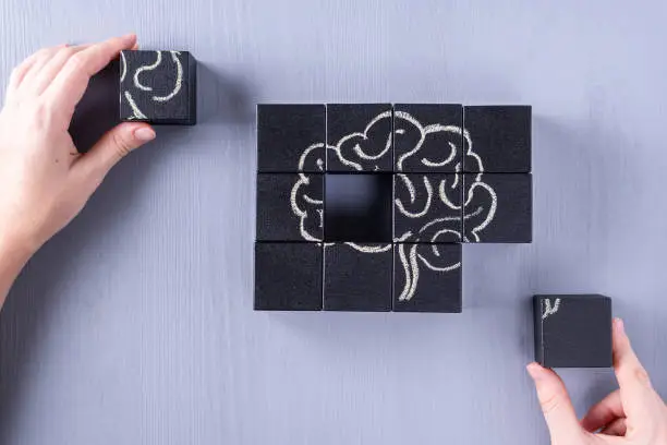 The concept of the human brain. Education, science and medical concept.  Brain drawn in chalk on black cubes.
Female hands put in place the last element of the puzzle.