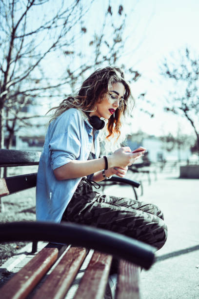 istock Cute Urban Girl Using Her Smartphone On a Park Bench 1129865232