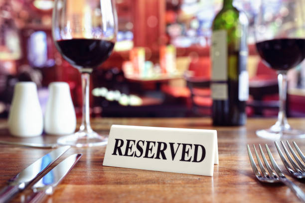 Reserved sign on restaurant table with bar background Restaurant reserved table sign with places setting and wine glasses ready for a party restaurant place setting dinner dinner party stock pictures, royalty-free photos & images