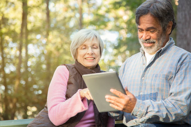 アクティブ シニアの大人のカップルは屋外デジタル タブレットを使用します。 - autumn senior adult mature couple active seniors ストックフォトと画像