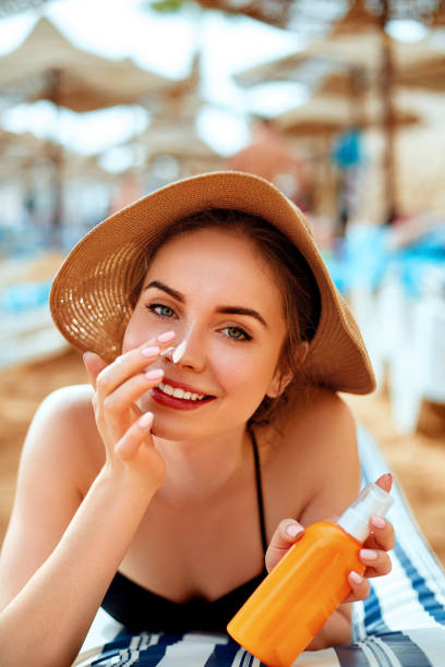 Sunscreen / sunblock. Woman putting solar cream on nose smiling  beautiful summer day. Skincare. Girl applying sun cream stock photo
