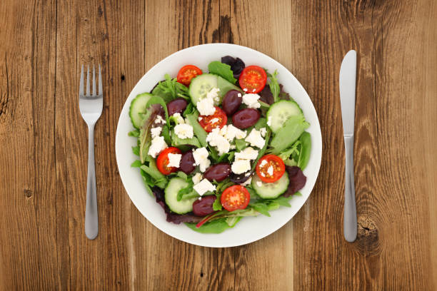 Greek salad with knife and fork on wooden background