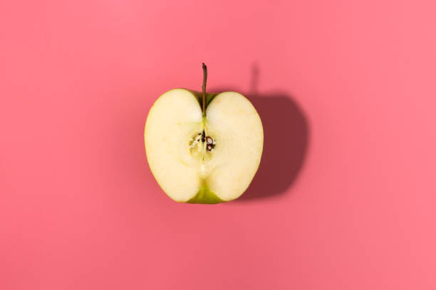 istock Sliced green delicious apple isolated on pink background with contrast shadows, flat lay 1129873081