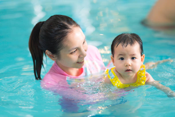 madre y niña asiáticos nadando en una piscina, clase de desarrollo temprano para los niños de natación. concepto de la natación del bebé. - bebe bañandose fotografías e imágenes de stock