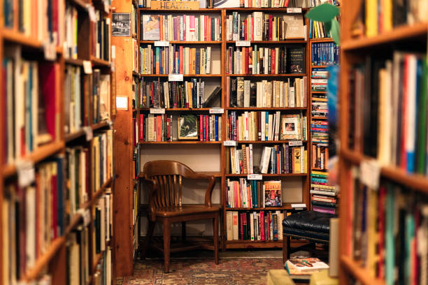 Books on display in the corner of a second hand bookstore An array of book titles under a variety of category headings on bookshelves above a wooden chair in the corner of a San Francisco second-hand bookstore. book shop stock pictures, royalty-free photos & images