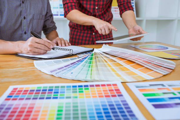 istock Teamwork of young creative designers working on project together and choose color swatch samples for selection coloring on digital graphic tablet at workspace 1129885392