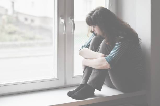 istock Sad young woman sitting on the window, watching out 1129891477