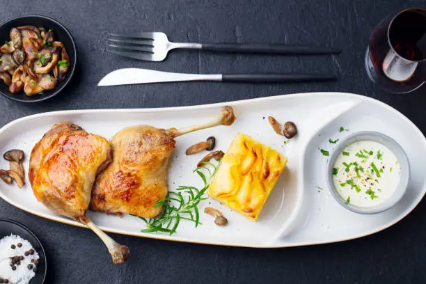 Photo of Duck legs confit with potato gratin and mushroom sauce. Restaurant serving. Top view.