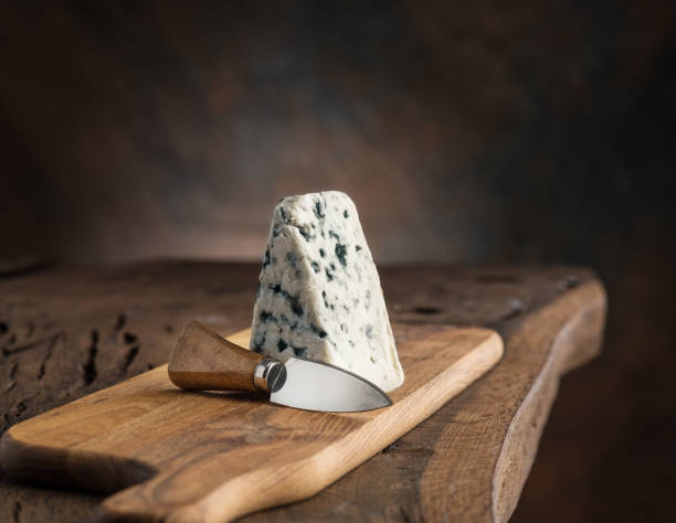 Piece of blue cheese and cheese knife on the wooden board. Dark background.
