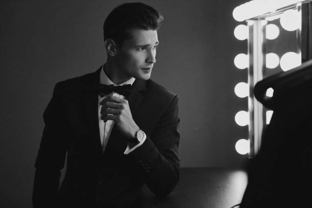 istock Sexy man in black suit looking at mirror 1129909281