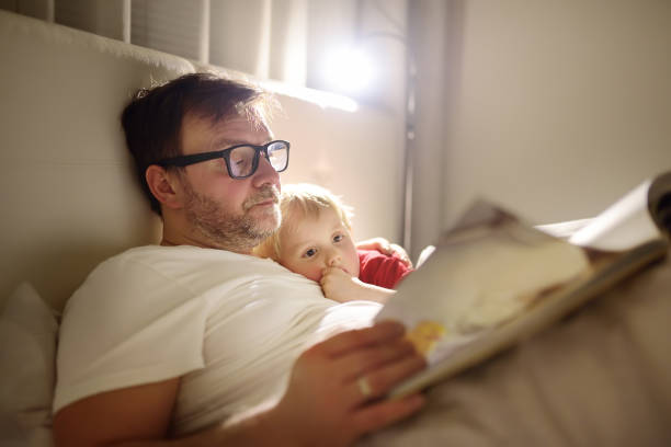 père, lisent des histoires enchantées avec enfants. fils de mettre papa de dormir - bedtime photos et images de collection