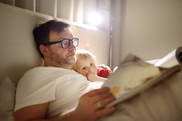 ojciec czyta dzieciom opowieści na dobranoc. tata kładąc syna do snu - snow glasses zdjęcia i obrazy z banku zdjęć