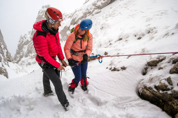 due alpinisti discutono delle procedure di discesa in corda doppia di sicurezza prima di scendere in corda doppia lungo una chutte innevata, su un difficile percorso invernale nei monti piatra craiului/carpazi, romania - cold discussion outdoors snow foto e immagini stock