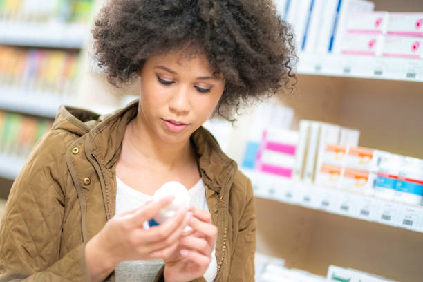 jovem mulher comprando em farmácia - vitamin pill nutritional supplement pill bottle - fotografias e filmes do acervo