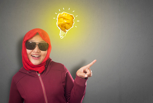 Portrait of successful beautiful Asian muslim woman smiling happy with bright light bulb lamp made of paper, symbol of idea creativity and innovation