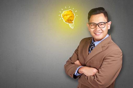 Portrait of successful handsome Asian man smiling happy with bright light bulb lamp made of paper, symbol of idea and innovation