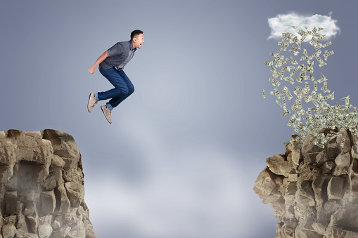 Businessman jumping off the mountain looking rain of money on the other side, risky job pursue wealth concept