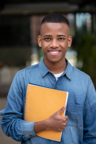 istock Portrait of handsome young college student holding his notebook while facing camera smiling 1129999666