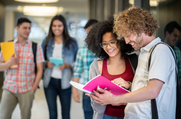 istock Cheerful diverse friends at college looking at a notebook studying before class smiling 1129999694