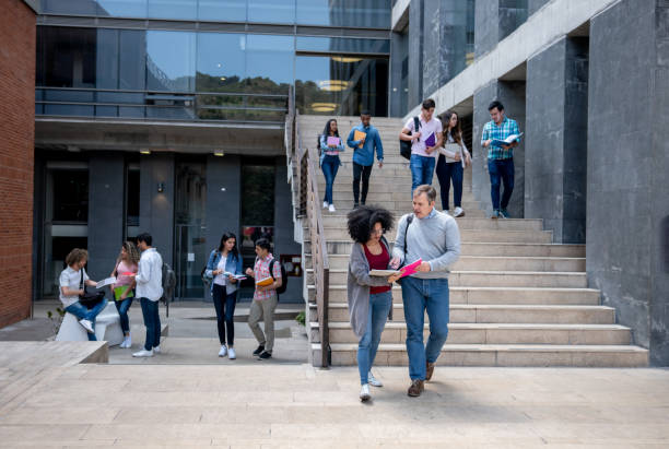 Students at the university campus walking to and from class and teacher helping a black female student while looking at a notebook